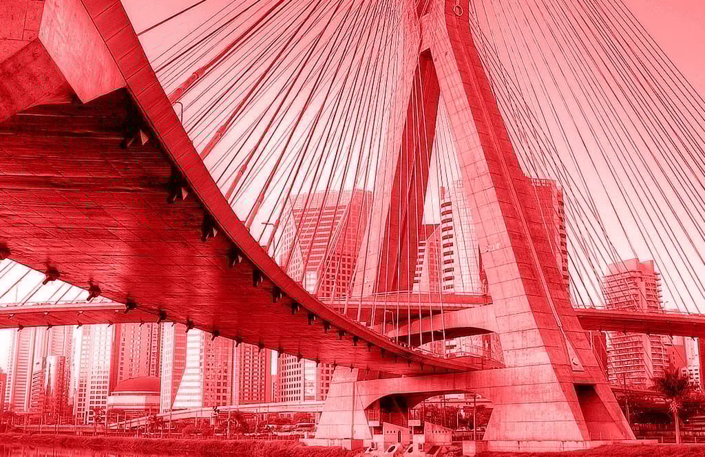 Ein Bild von Sao Paulo von einer großen Schrägseilbrücke mit mehreren Kabeln und massiven Betonpfeilern. Im Hintergrund sind hohe Gebäude einer modernen Skyline zu sehen.