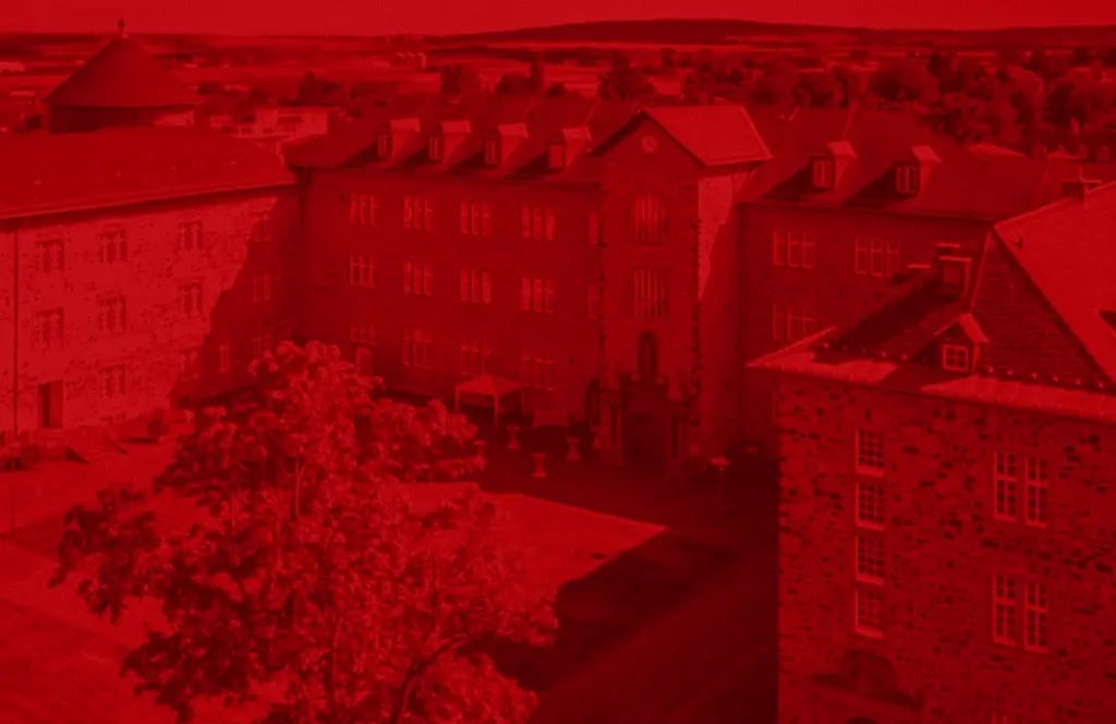 Ein historisches Schlossgebäude mit mehreren Flügeln und einem Innenhof. Im Vordergrund stehen Bäume, im Hintergrund ist eine weite Landschaft sichtbar.