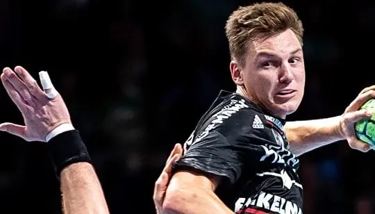 Handballspieler in schwarzem Trikot springt mit Ball in der Hand